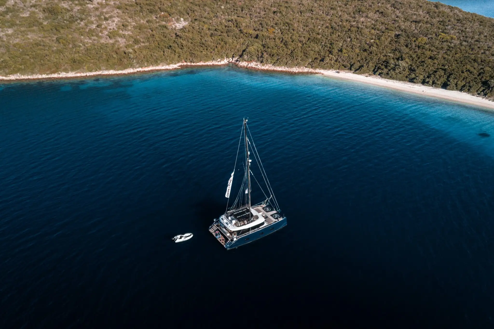 A crewed catamaran at anchor in a turquoise bay in the Ionian Islands, Greece