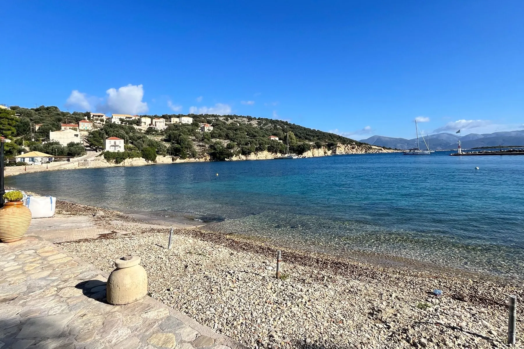 Kastos - Oasis Sailing The pebble shore at Kastos, a scatter of white houses along the water and the bay opening beyond